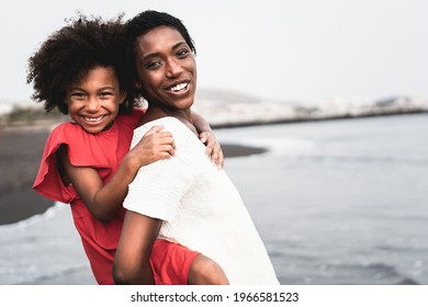 Black mother and daughter having fun on the beach at sunset time during summer vacation - Focus on mother face