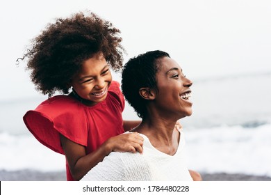 Black mother and daughter running on the beach at sunset time during summer vacation - Family people having fun together outdoor - Travel and happiness lifestyle - Focus on mom's face