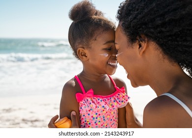 Black Mother Embracing Daughter With Sunscreen On Face At Beach. Woman Rubbing Nose Face To Face With Her Cute Little Girl With Sun Lotion On Cheek. Funny Black Female Kid With Sunblock At Seaside.