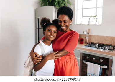 Black mother holding her daughter in her warm arms as she says goodbye on a school morning. Happy parent showing her child love and affection, preparing her for the day ahead.