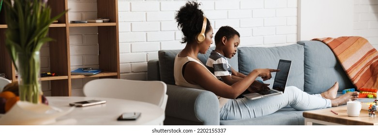 Black Mother And Son Using Laptop While Sitting On Sofa At Home