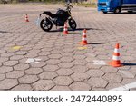 A black motorcycle is parked in a parking lot with a row of orange cones in front. Motorcycle driving school concept.