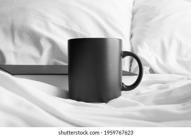 Black Mug Mockup With A Book On The Bed.