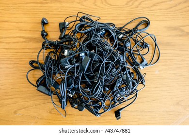 A lot of black music earphones pile together as a electronics waste on the wood background