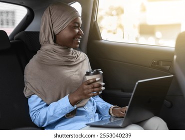 Black muslim businesswoman in hijab riding to office with laptop and coffee on backseat, african islamic lady in headscarf enjoying road ride, having private transfer or using taxi service, free space - Powered by Shutterstock