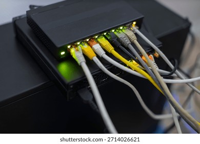 A black network switch is shown with several colorful ethernet cables plugged into its illuminated ports, indicating active data connections.
