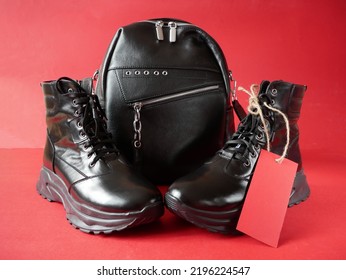 Black New Woman Or Man Rough Pair Of Boots And Backpack With A Tag For The Inscription From The Sale On A Red Background, Autumn And Winter Sale Concept