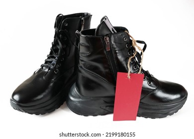 Black New Woman Or Man Rough Pair Of Boots With A Tag For The Inscription From The Sale Isolated On A White Background, Autumn And Winter Sale Concept