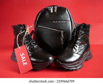 Black New Woman Or Man Rough Pair Of Boots And Backpack With A Tag For The Inscription From The Sale On A Red Background, Autumn And Winter Sale Concept