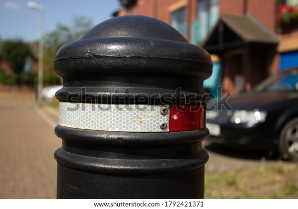 black no entry bollard with red\
and white reflectors with a car and houses in the\
background