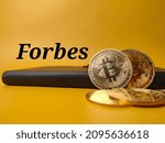 Black notebook and bitcoins with text Forbes on a yellow background.