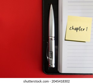Black notebook, pen on red background with copy space and stick note written CHAPTER 1, concept of start writing book - novel fiction non-fiction  first time writer get start, writing for extra income