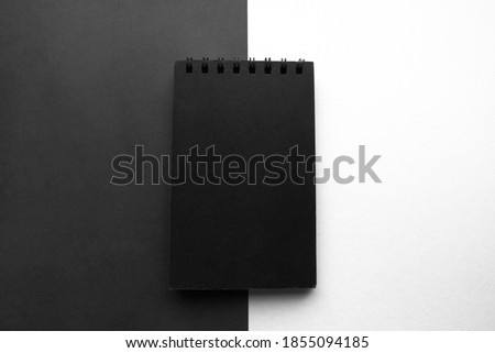 Black notepad on black and white divided in half background with space for text. Copy space. Top view. Minimalistic design concept