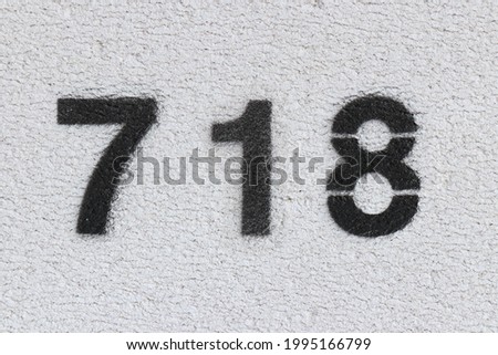 Black Number 718 on the white wall. Spray paint. Number seven hundred and eighteen.