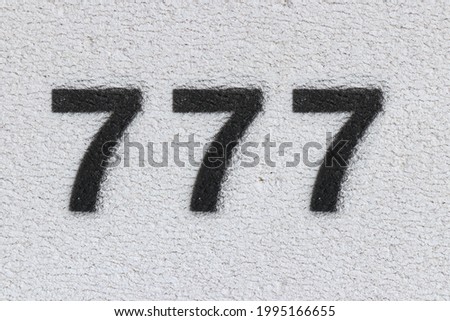 Black Number 777 on the white wall. Spray paint. Number seven hundred and seventy seven.