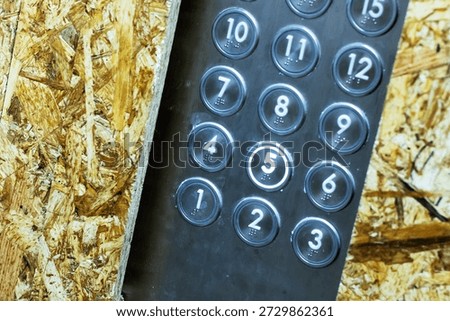 black numeric keypad on rough plywood, closeup showing scuffed circular buttons labeled  and weathered OSB texture,