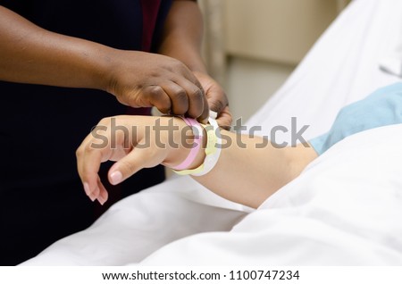 A black nurse assisting a white lady upon admission with her admission bracelets while she waits for her scheduled c-section