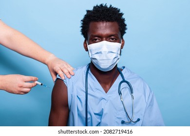 Black Nurse Getting Vaccinated With Syringe And Needle While Wearing Face Mask. African American Healthcare Assistant Receiving Vaccine Shot From Hands Of Doctor For Virus Protection