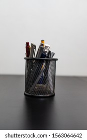 Black office pot with pencils and pens on a white background. Metal pen pot on black desk.
