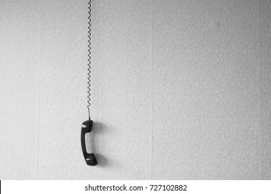 Black Old Handset With A Wire Hang Against Wallpaper Texture. Black Plastic Telephone Hanging By The Cord.Retro Phone Cord - Vintage Telephone Handset Receiver Hanging By The Cord Down