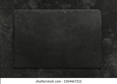 Black on black. Empty black granite stone rectangle board on black textured cement background, top view vith copy space for your text.