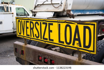 Black On Yellow Oversize Load Sign Installed On The Back Of Big Rig Semi Truck Tractor With Heavy Metal Bumper For Safety Moving Stand On The Parking Lot Awaiting For The Next Oversized Cargo