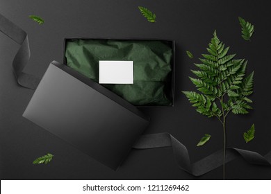 Black open box mockup and stationery set, top view, with floral elements, flowers and blank copy space on black background.