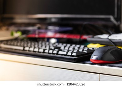 Black Optical Mouse And Blurred Keyboard On Messy White Computer Desk.