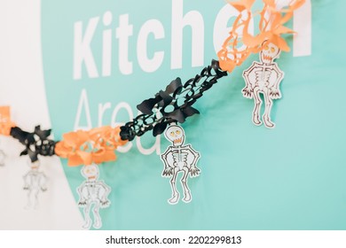 Black Orange Paper Skeletons Garland On Green Wall. Halloween Decoration Of Corporate Office Kitchen Area. Front View, Selective Focus.