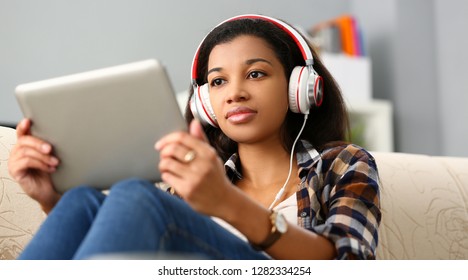 Black Ordinary Female American Teen Portrait At Home Sofa Remote Education Concept. Girl Hold Tablet In Hand Music Apps Teacher Checks Homework Online University Library Learning Foreign Languages