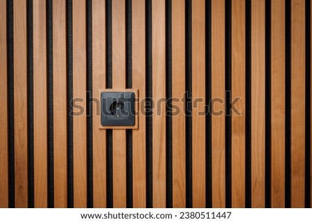 Black outlet plug on the wooden wall. Socket and European Power in the New Flat. Acoustic fluted wood panel.