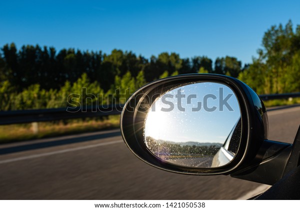 Black oval mirror car reflecting sun shining on\
a blue landscape