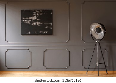 Black painting on grey wall with molding in dark apartment interior with lamp. Real photo. Paste your sofa here
