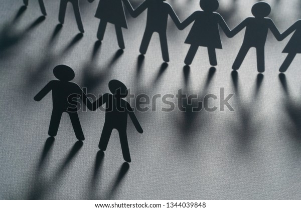 Black paper figure of a male couple\
in front of a crowd of paper people holding hands on white surface.\
Social movement, protest, leadership\
concept.