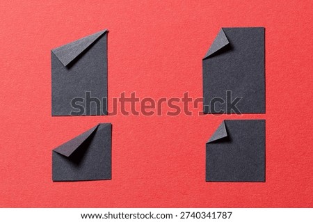 Black paper message notes or sheets with folded edge dog-ear earmark and copy space for text on red background, top view flat lay conceptual desk backdrop