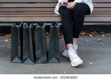 Black Paper Shopping Bags Next To Womens Feet In Sneakers. Fashion Shopping. Woman After Shopping.