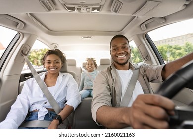 Black Parents And Daughter Posing Riding New Car Smiling To Camera Enjoying Road Trip. Family Having Vacation Traveling Together By Auto. Automobile Purchase Concept. Selective Focus