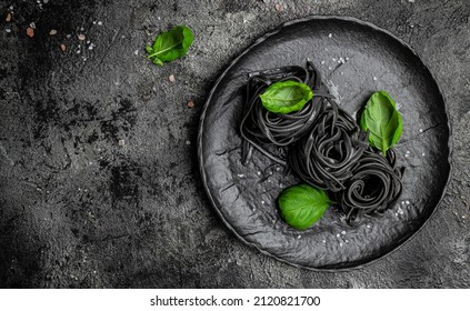 black pasta with cuttlefish ink and green basil leaves. Pasta of durum wheat semolina with squid ink. Restaurant menu, dieting, cookbook recipe top view.