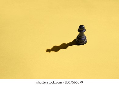 Black pawn with kings shadow on yellow background