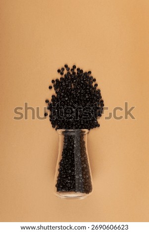 Black PE pellets. Black masterbatch or Polyethylene granules scattered out of glass lab flask. Granulated plastic compound. Virgin polymer.
