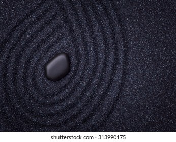 Black pebble in a zen garden with wave lines in the black grain sand  - Powered by Shutterstock