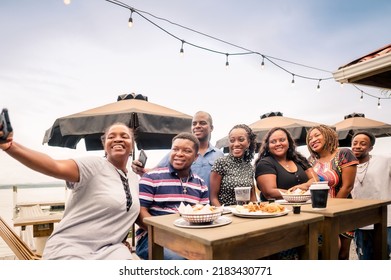 Black People Taking A Selfie With Their Cell Phones Having A Good Time. African-American Family Enjoying A Meal At A Beach Restaurant.