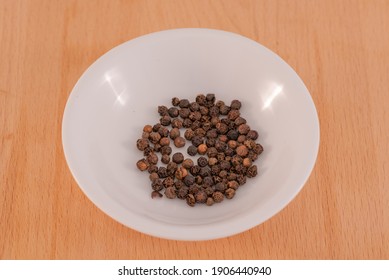 Black Pepper Corns in a white bowl on a chopping board background