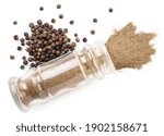 Black peppercorns and ground pepper in a glass bottle close-up on a white background, isolated. Top view