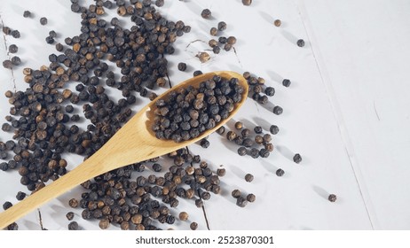 Black peppercorns scattered on a white wooden surface with a wooden spoon, showcasing spices for cooking, in a clean and minimal food presentation - Powered by Shutterstock