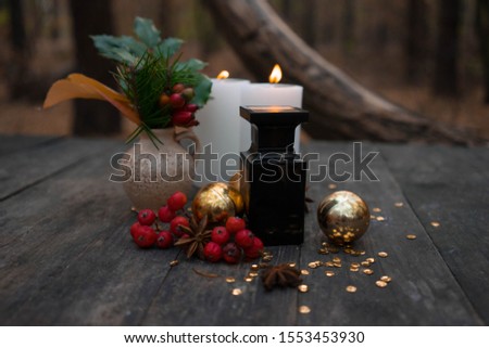 black perfume bottle with burning candles, a small vase with green holly, red berries and anise stars with golden balls
