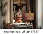 Black person artist, surrounded by paintings, working in cozy home studio with plants and wooden walls. Painting on easel shows a vibrant, abstract design