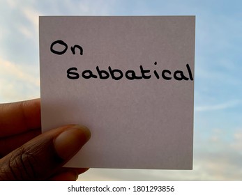 A Black person holding a handwritten note stating on sabbatical with the sky in the background  - Shutterstock ID 1801293856