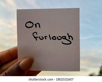 A Black Person Holding A Note Stating On Furlough With The Sky In The Background 