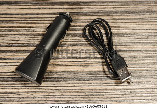 Black phone adapter for a car with a cable on\
the wooden table background. Charge your device on the way in the\
automobile.